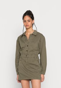 Vestido verde oliva de mangas longas com colarinho, fecho de botões à frente, cintura cingida e costuras anguladas. Feito de um tecido durável com um acabamento texturizado.