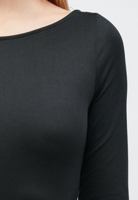 Fekete hosszú ujjú felső sima, rugalmas anyagból, széles, kerek nyakkivágással és testhezálló fazonnal, amely kiemeli a törzset.