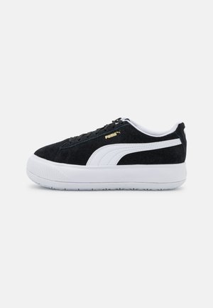 Baskets en daim noir avec accents blancs, présentant un dessus texturé, des lacets plats et une épaisse semelle en caoutchouc blanc. Détail logo doré sur le côté.