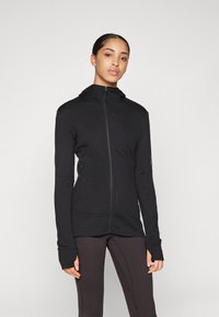 Melnā jaka ar rāvējslēdzēju, kapuci, garām piedurknēm, sānu kabatām un pieguļošu dizainu. Izgatavota no mīkstas auduma ar gludu tekstūru.