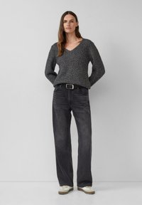 Gestrickter grauer Pullover mit V-Ausschnitt und strukturiertem Muster, kombiniert mit dunkelgrauen, geraden Jeans und hellbeigen Sneakers.