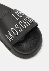 Black slide sandal featuring a textured strap with "LOVE MOSCHINO" in metallic rhinestones. Smooth footbed with a rounded shape.