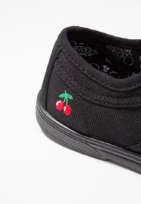 Sneaker in tessuto nero con profilo basso. Presenta un motivo di ciliegia ricamato rosso di lato e una soletta in gomma texturizzata.
