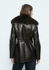Čierna kožená bunda s textúrovaným, tmavým kožúškom. Prispôsobený strih s vertikálnymi švami, siahajúcimi po boky. Hladký povrch.