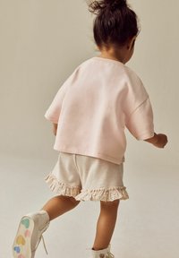 Ljusrosa oversized sweatshirt med korta ärmar, parat med beige shorts med volangkant. Vita stövlar med färgglada detaljer.