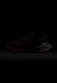 Bottine de course Nike noire avec logo swoosh orange, tige en mesh respirant et semelle rembourrée, présentée en faible lumière sur fond sombre.
