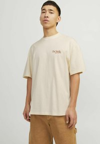 Crème-kleurige oversized t-shirt, van katoen, ronde halslijn, korte mouwen, met 'The Studio' in roestkleurige tekst op de borst gedrukt.