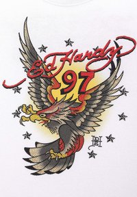 Bílý tričko s barevným grafickým potiskem ve stylu tetování, zobrazujícího orla s roztaženými křídly, hvězdami a nápisem "Ed Hardy 97" tučným červeným písmem.