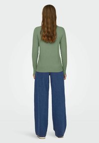 Grön långärmad tröja i mjukt material, kombinerad med hög midja och vida blå jeans. Tyget ser slätt ut med en åtsittande silhuett.