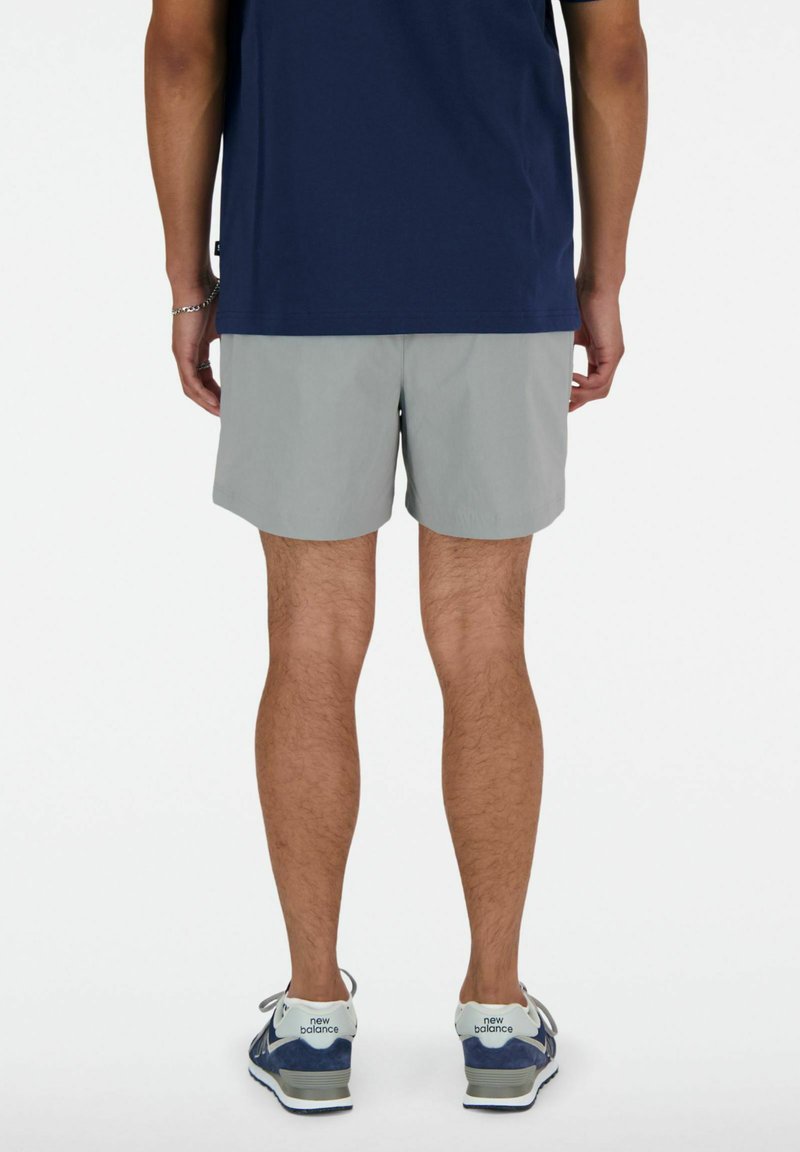 Pantalones cortos grises de un color sólido, llevados con una camisa azul marina. Presentan un ajuste cómodo y se combinan con zapatillas azules y blancas.
