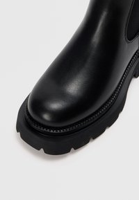 Zwarte leren enkellaars met een ronde neus, een gestructureerde bovenkant, een contrasterende chunky rubberen zool en gedetailleerde stiksels langs de rand.