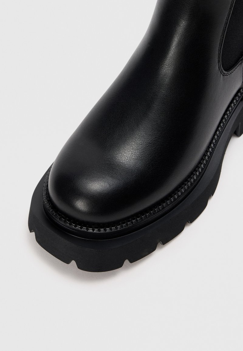 Stivale alla caviglia in pelle nera con punta tondeggiante, tomaia testurizzata, suola in gomma spessa a contrasto e cuciture dettagliate lungo il bordo.