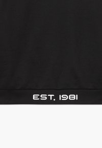 Sudadera negra con dobladillo acanalado y texto blanco que dice "EST. 1981." Diseñada con una textura suave y una silueta clásica.