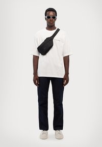 White oversized t-shirt, black crossbody bag, dark jeans, and white sneakers. Accessories include black sunglasses. Simple and casual outfit.