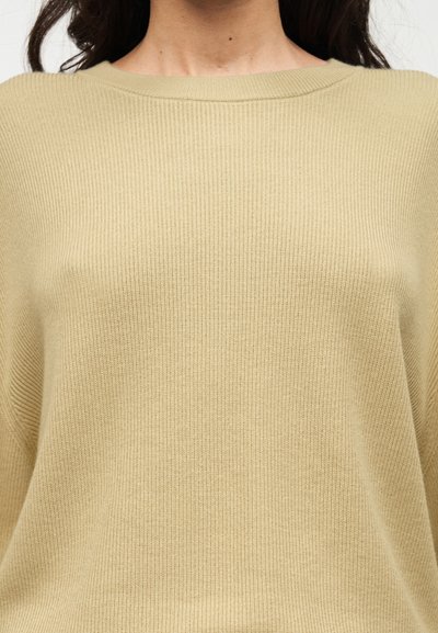 Pull beige clair à côtes avec un large décolleté, une texture douce et une coupe ample, doté de manches longues et de détails de design minimalistes.