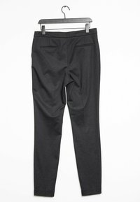 Zwarte op maat gemaakte broek met een gestructureerd patroon, slim fit, zakken aan de achterkant en een soepele tailleband. Hangt aan een zwarte plastic hanger.