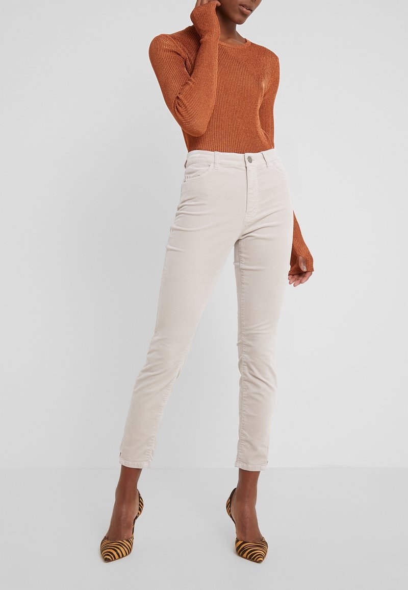 Helle beige Cordhose im Slim-Fit, kombiniert mit einem gerippten, rost-orangefarbenen Langarmtop und gestreiften High-Heels.