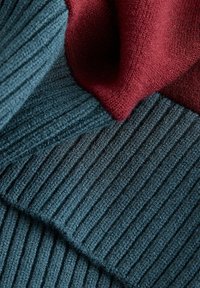 Dwa kawałki materiału: jeden prążkowany dzianinowy w kolorze morskim, drugi gładki w bordowym kolorze, ułożone warstwowo i częściowo złożone, ukazujące kontrast tekstury i koloru.