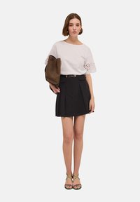 Camisa blanca con mangas de encaje, combinada con una falda corta plisada negra y sandalias verdes con tiras. Bolso marrón con textura perforada.
