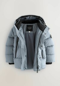 Veste matelassée bleu clair avec un intérieur noir, poches zippées et une étiquette de logo. Tissu texturé avec une finition lisse.