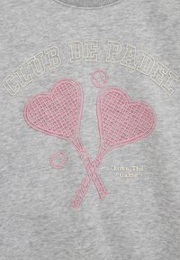 Hall hallipluus, millel on helekollakas kiri "CLUB DE PADEL", kaks roosat padel reketit südamekujulises kujunduses ning allosas kreemikas kirjas "Love The Game".