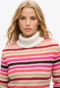 Pull rayé avec un col montant côtelé blanc. Présente des lignes horizontales en rose, rouge, beige et marron, fabriqué en maille texturée.