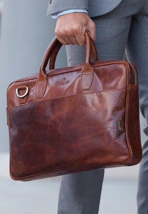 Brown leather briefcase with dual top handles, zip closure, and a smooth finish. Features a front pocket and metal accent.