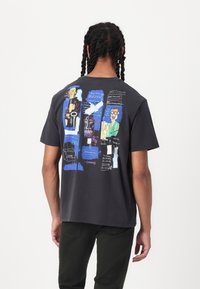 Cotton t-shirt in dark gray featuring a colorful, abstract graphic design on the back. Short sleeves and a standard fit.