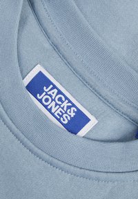 Collare in cotone azzurro chiaro con texture a maglia piatta, dotato di un'etichetta del marchio JACK & JONES bianca e blu sul lato interno.