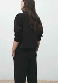 Sweatshirt noir avec une coupe décontractée, des poignets côtelés et un col haut, associé à un pantalon noir assorti. Texture lisse, design minimal.