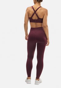 Sostenedor deportivo burdeos y leggings de cintura alta a juego, confeccionados en una tela suave, con tirantes en la parte posterior cruzados y costuras contorneadas.