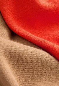 Close-up of soft knitted fabric folds in bright orange and beige colors with visible texture and fine fibers.