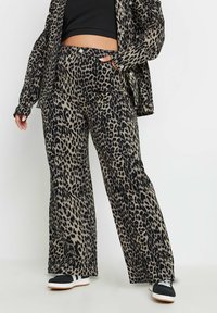 Pantalones de pierna ancha con estampado de leopardo en una tela suave, con cintura elástica, bolsillos laterales y combinados con zapatillas negras.