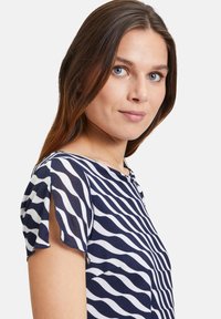 Marineblau und weiße Bluse mit welligem Muster, kurzen Ärmeln, rundem Halsausschnitt und weichem Stoff, mit asymmetrischem Saum.