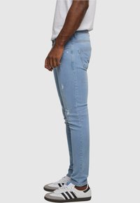 Világoskék, slim fit farmernadrág, szakadt részletekkel, öt zsebes dizájnnal. Fehér sportcipő, fekete csíkokkal és szürke talppal párosítva.