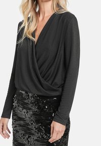 Svart långärmad topp med djup V-ringning och draperad front, kombinerad med en figurnära svart paljettkjol. Båda har en texturerad finish.