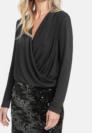 Haut noir à manches longues avec un décolleté en V plongeant et un devant drapé, associé à une jupe moulante en sequins noirs. Les deux présentent une finition texturée.