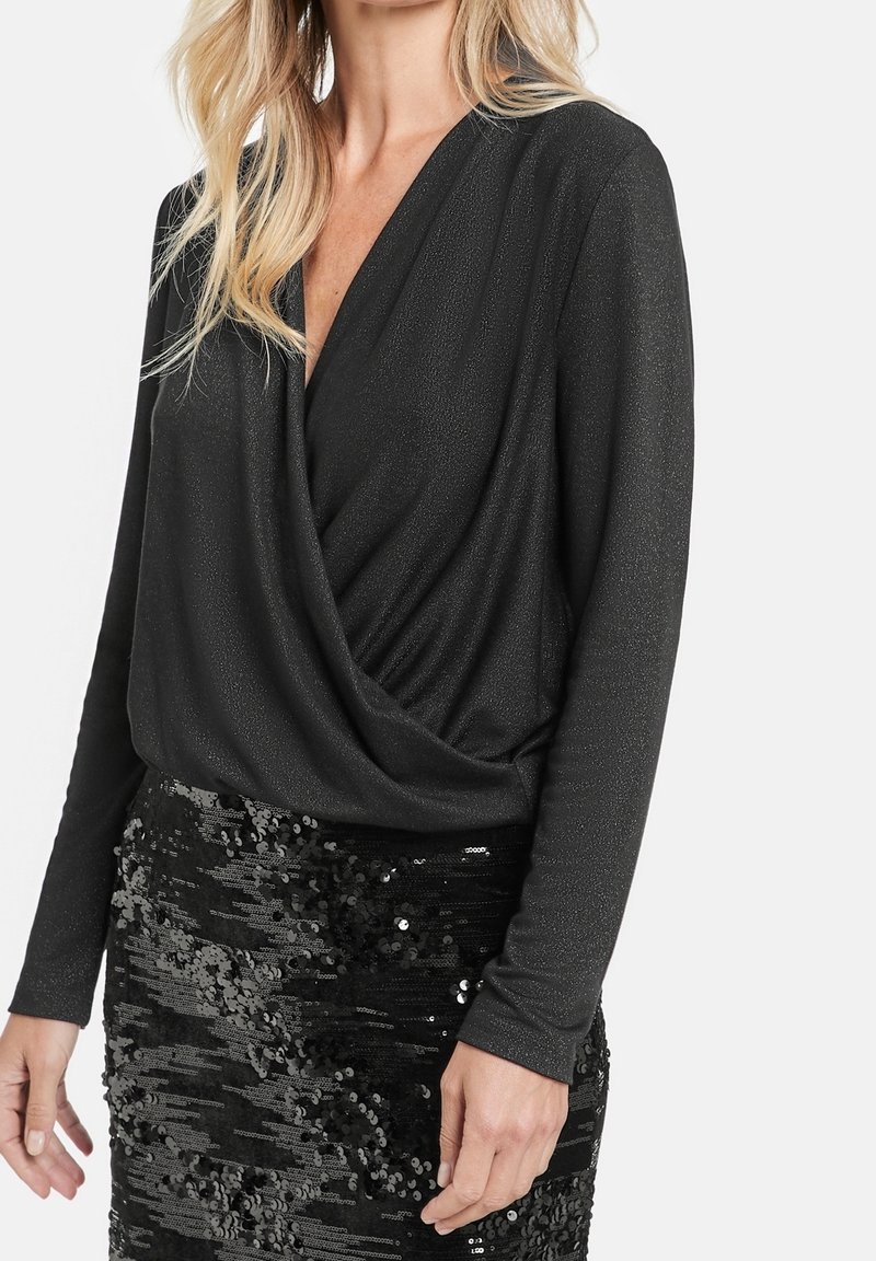 Svart långärmad topp med djup V-ringning och draperad front, kombinerad med en figurnära svart paljettkjol. Båda har en texturerad finish.