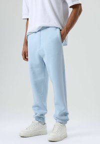 Lichtblauwe joggingbroek met elastische boorden en zakken, gemaakt van zachte stof. Draagt met een wit T-shirt en witte sneakers.