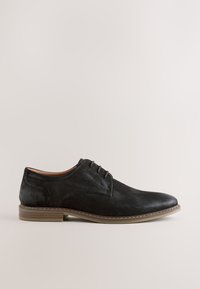 Chaussure habillée pour homme en daim noir à lacets, semelle couleur cuir clair et petit talon empilé, vue de côté extérieur sur fond uni.