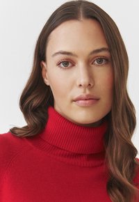 Pulover roșu cu guler înalt, confecționat dintr-un tricot moale, având un guler și manșete striate, cu o textură netedă și un design minimal.