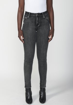 Jean skinny noir avec un délavage, design à cinq poches et coutures décoratives sur le devant. Porté avec des bottines noires.