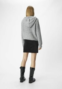 Grå stickad hoodie med avslappnad passform och huva, kombinerad med en svart manchester mini kjol och knähöga svarta blanka stövlar.