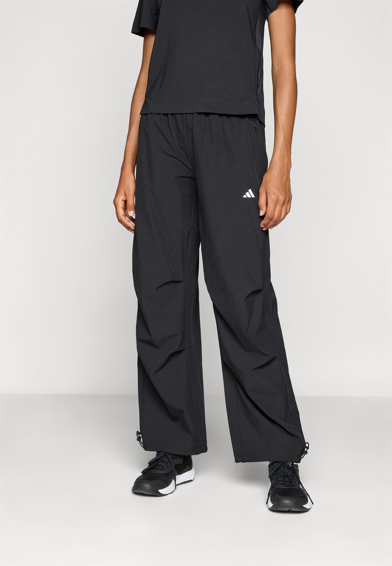 Zwarte sportoutfit met een Losse T-shirt en brede broek. De broek heeft een elastische tailleband en ritsdetails aan de zoom.