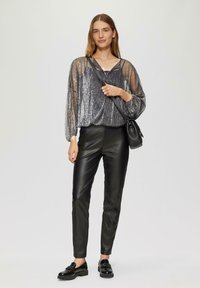 Haut en argent brillant et texturé avec des manches longues et un décolleté en V, associé à un pantalon en cuir noir ajusté et des chaussures noires. Petit sac bandoulière noir.