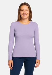 Maglia manica lunga viola a coste con scollatura rotonda e design aderente, abbinata a jeans blu scuro. Texture liscia in tutto il capo.