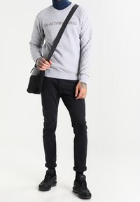 Felpa trapuntata grigia con logo "G-Star RAW", abbinata a jeans neri e sneakers nere. Include una borsa a tracolla nera.