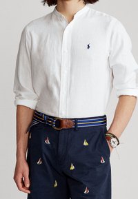 Vit linneskjorta med ståkrage, matchad med marinblå byxor med färgglad segelbåt-broderi och ett flerfärgat randigt bälte.