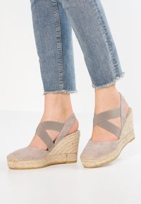Béžové wedges s juty platformou, s křížovými elastickými pásky a měkkým nubukem. Džíny s třepeným lemem doplňují obuv.