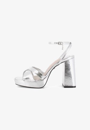 Sandalias de plataforma plateadas con tiras anchas cruzadas y una correa con hebilla en el tobillo. Cuenta con un tacón cuadrado grueso y un acabado metálico texturizado.
